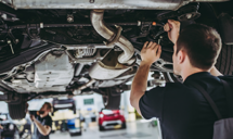 Un homme est sous une voiture qui est surélevée, pour la réparer